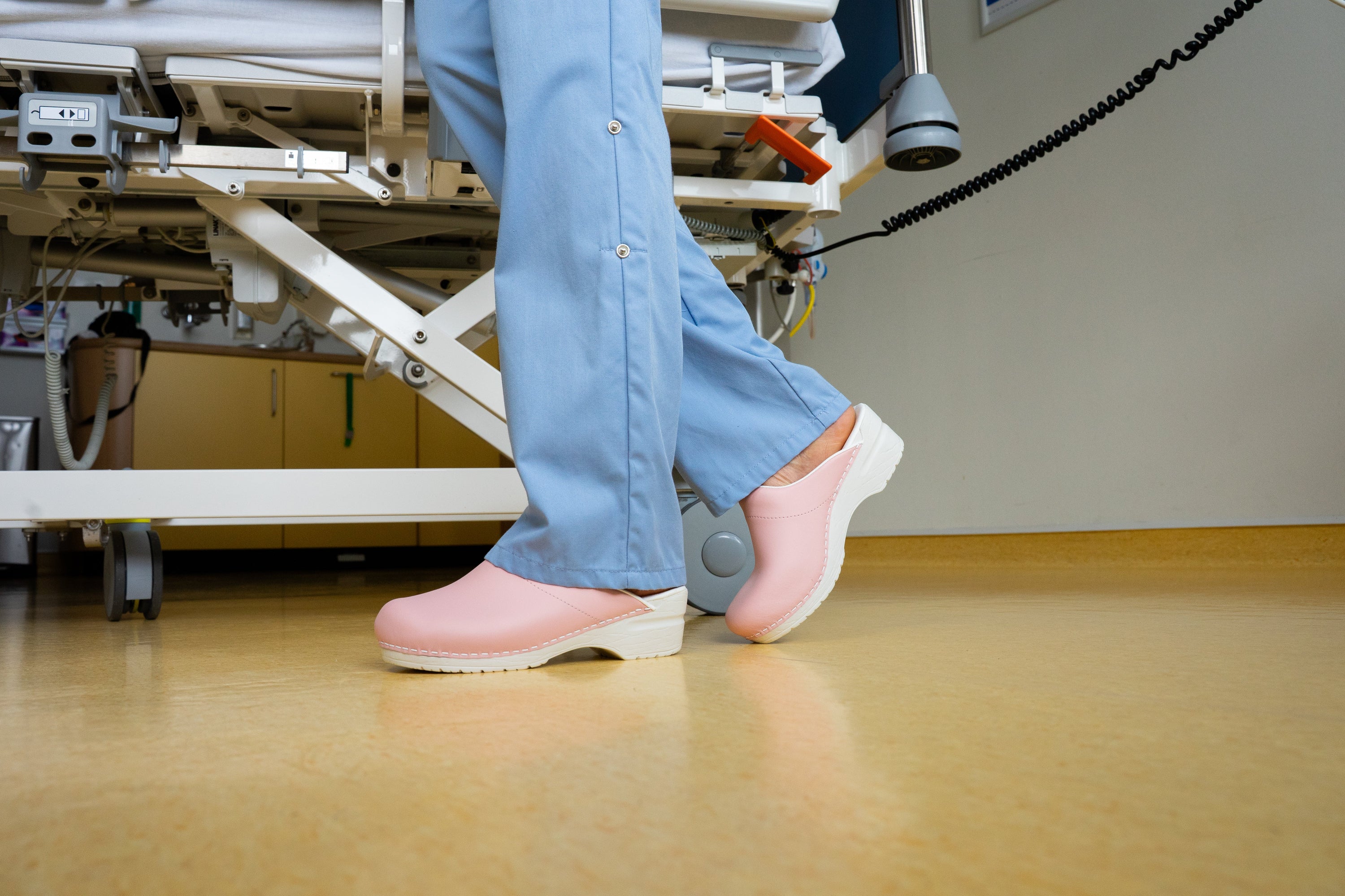 Verpleegkundige met roze medische klompen op een ziekenhuisafdeling